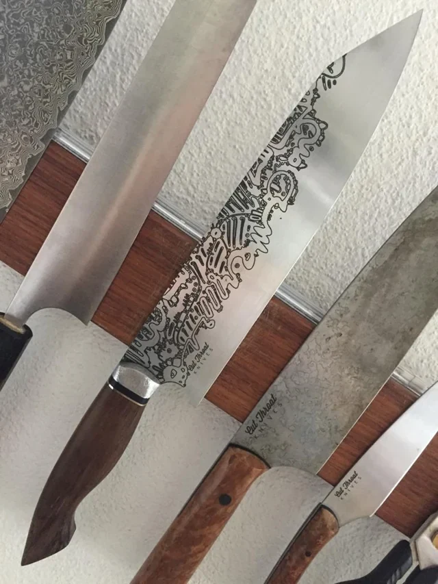 Knives on a wall rack, including a blade with engraved line graphics.