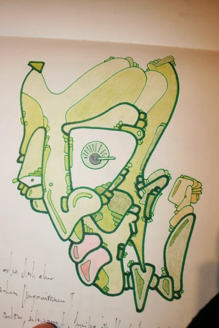 A green and pale yellow stylised face in an open sketchbook.